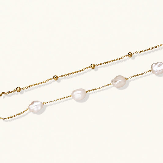 Double-strand gold bracelet with irregular baroque pearls and smooth freshwater pearls on cream background.