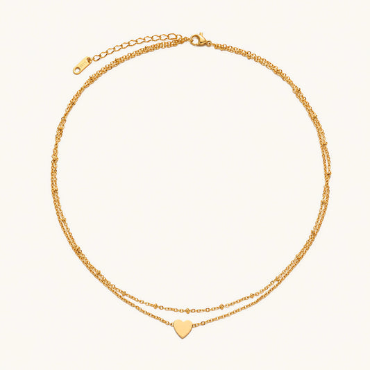 Delicate double-chain gold necklace with tiny heart pendant on cream background