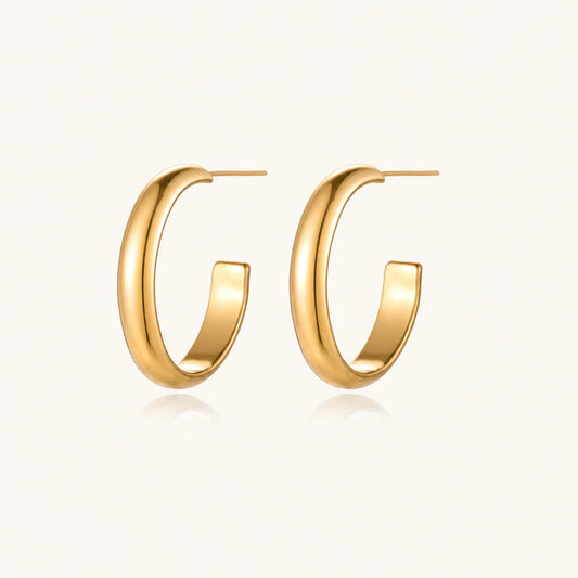 Chunky tubular hoop earrings in warm 14K gold-plated finish with smooth polished surface on cream background.