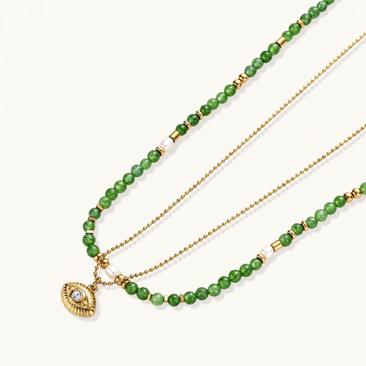 Layered necklace with green stone beads, gold spacers, white accents, and protective eye pendant on cream background.