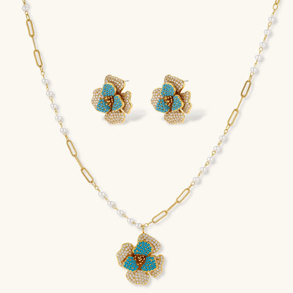 Gold-plated flower jewelry set with blue zirconia center petals and clear crystal outer petals on neutral background.