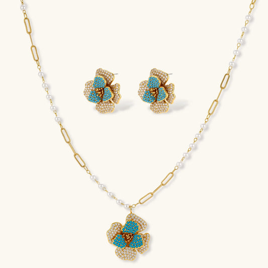 Gold-plated flower jewelry set with blue zirconia center petals and clear crystal outer petals on neutral background.