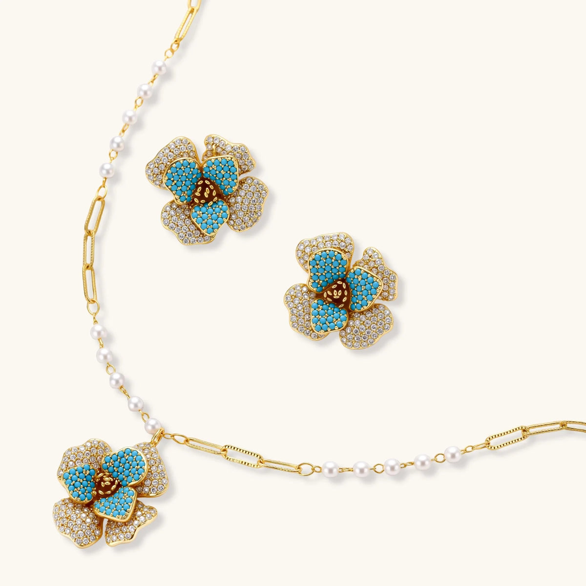 Gold-plated flower jewelry set with blue zirconia center petals and clear crystal outer petals on neutral background.