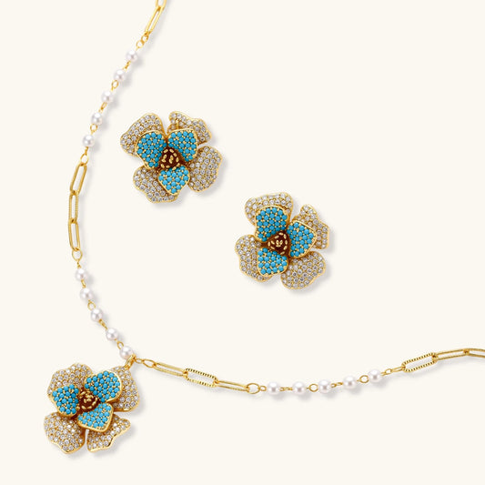 Gold-plated flower jewelry set with blue zirconia center petals and clear crystal outer petals on neutral background.