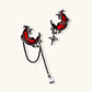 Gothic asymmetrical earrings with red crescent moons, black dripping stars, chains and crystal drop on white background.