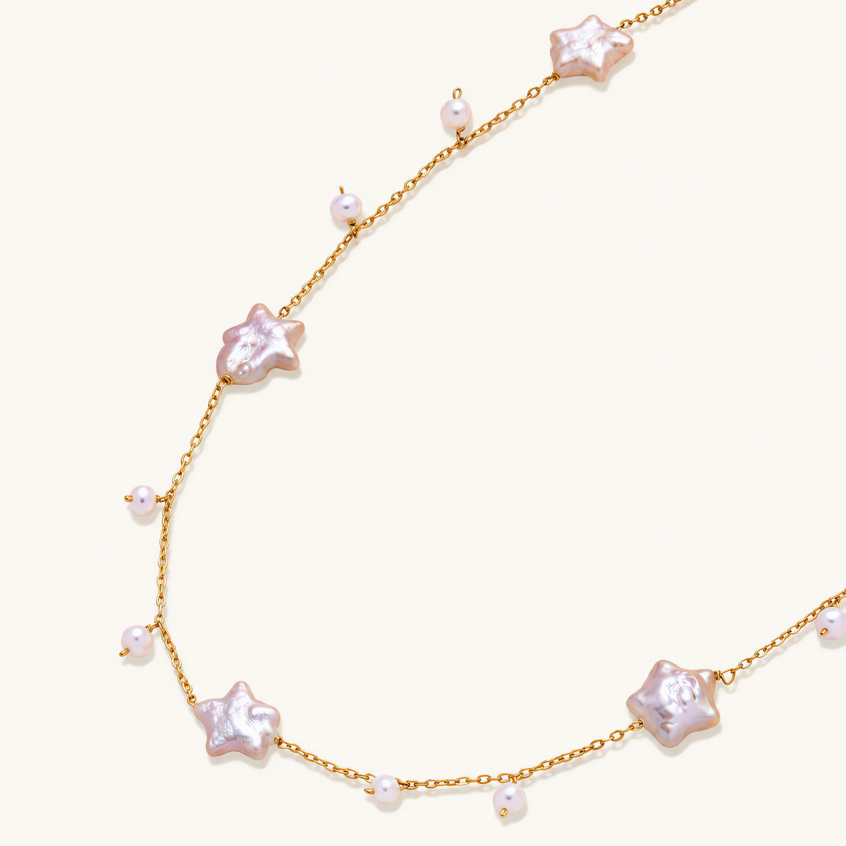 Gold vermeil chain with iridescent star-shaped baroque pearls and small round freshwater pearl drops on cream background.