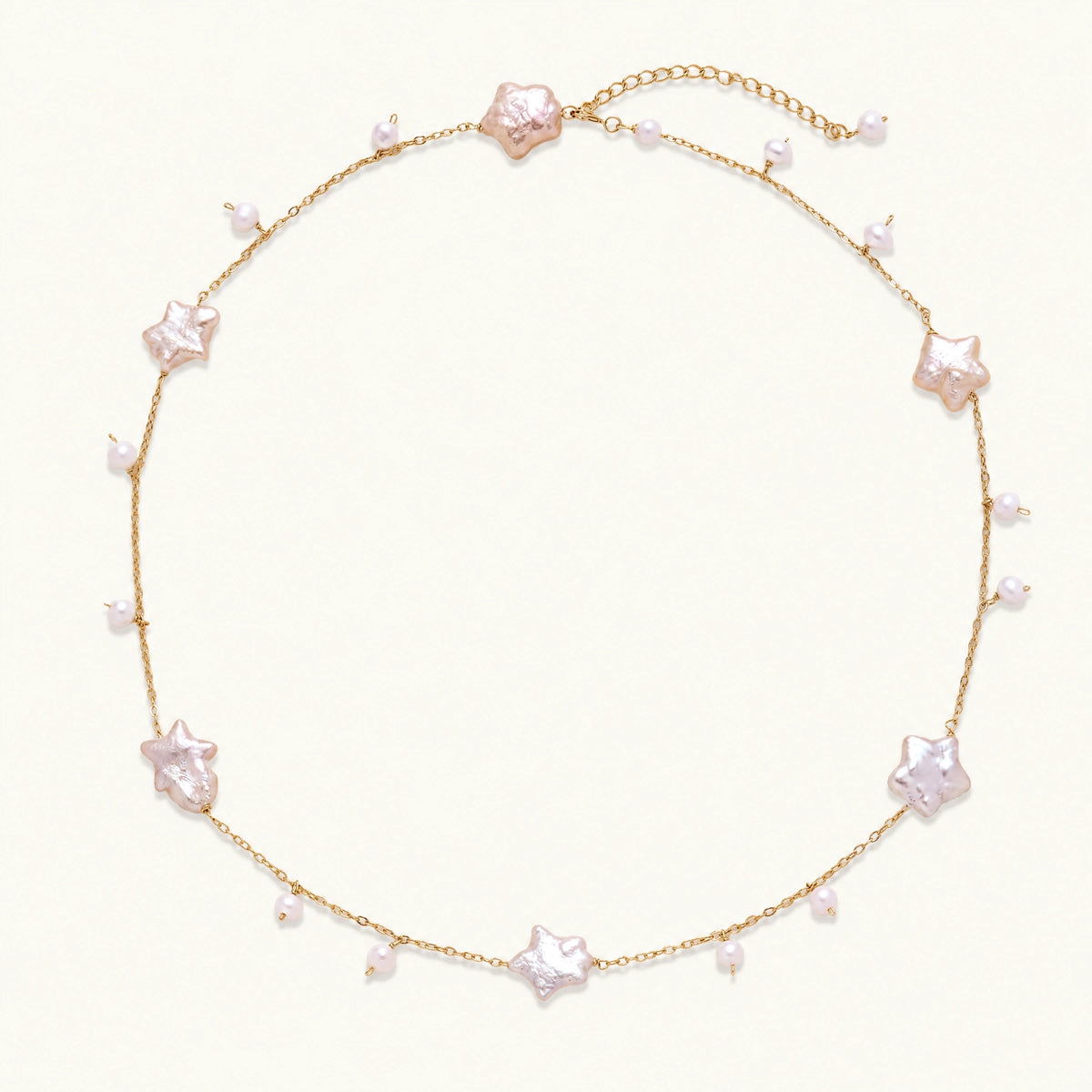 Gold vermeil chain with iridescent star-shaped baroque pearls and small round freshwater pearl drops on cream background.