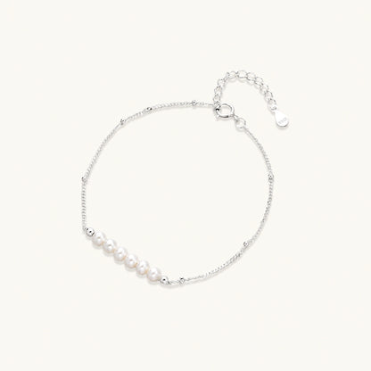 Delicate rhodium-plated silver chain bracelet with row of small baroque pearls centered on white background.