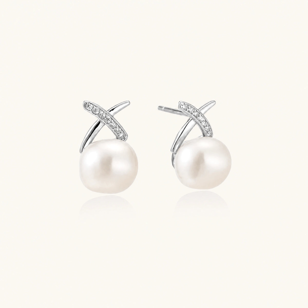 Rhodium-plated silver stud earrings with sparkling X design above lustrous round freshwater pearls on white background.