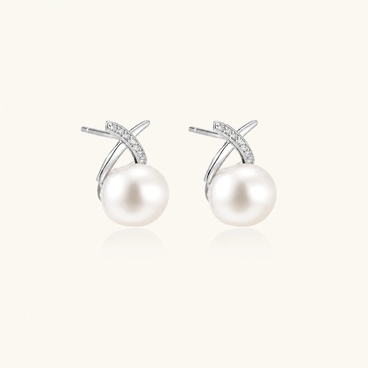 Rhodium-plated silver stud earrings with sparkling X design above lustrous round freshwater pearls on white background.