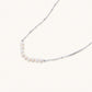 Delicate sterling silver chain necklace with small freshwater pearls arranged in a curved smile arc on cream background.