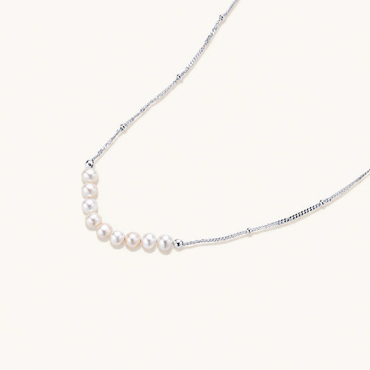 Delicate sterling silver chain necklace with small freshwater pearls arranged in a curved smile arc on cream background.