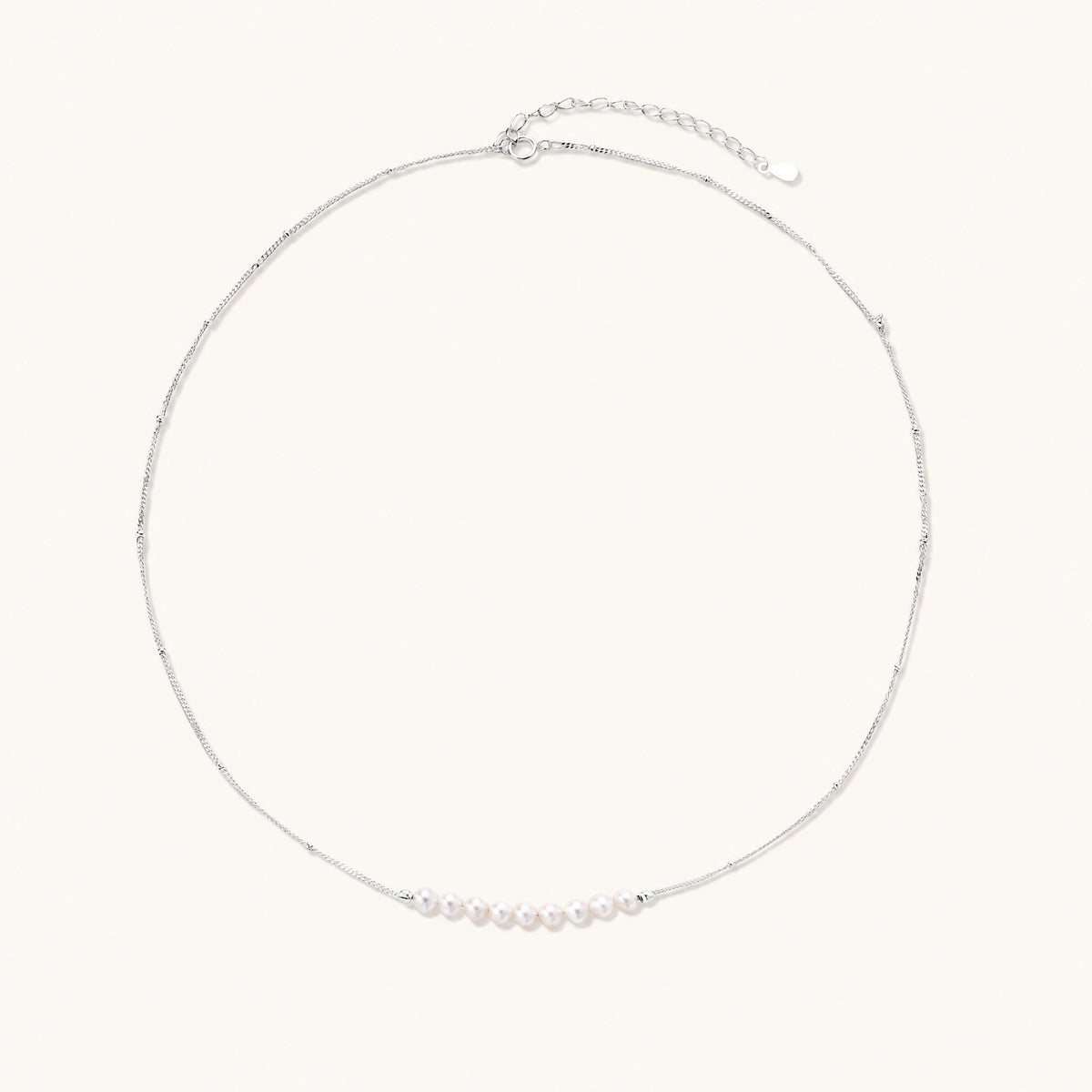 Delicate sterling silver chain necklace with small freshwater pearls arranged in a curved smile arc on cream background.