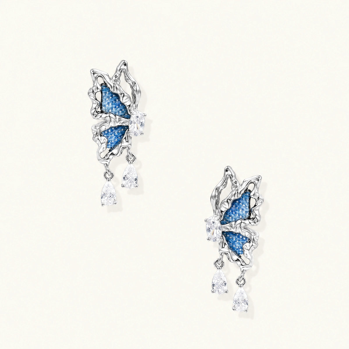 Silver butterfly earrings with blue denim fabric wings and dangling teardrop crystals on cream background