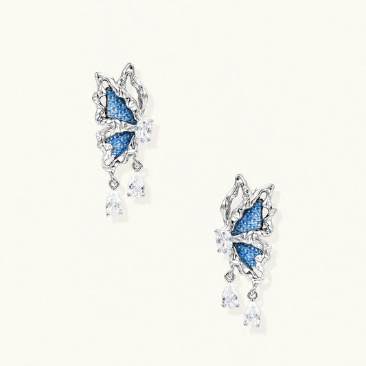Silver butterfly earrings with blue denim fabric wings and dangling teardrop crystals on cream background