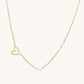 Dainty 14K gold plated stainless steel necklace with an open heart charm and a single round white bead on a cream background.
