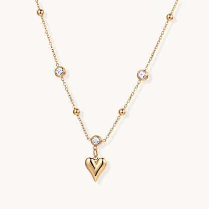 Delicate gold-plated necklace with bezel-set crystals and small heart pendant on beige background