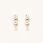 14K gold-plated curved stud earrings with three white freshwater pearls aligned vertically on cream background