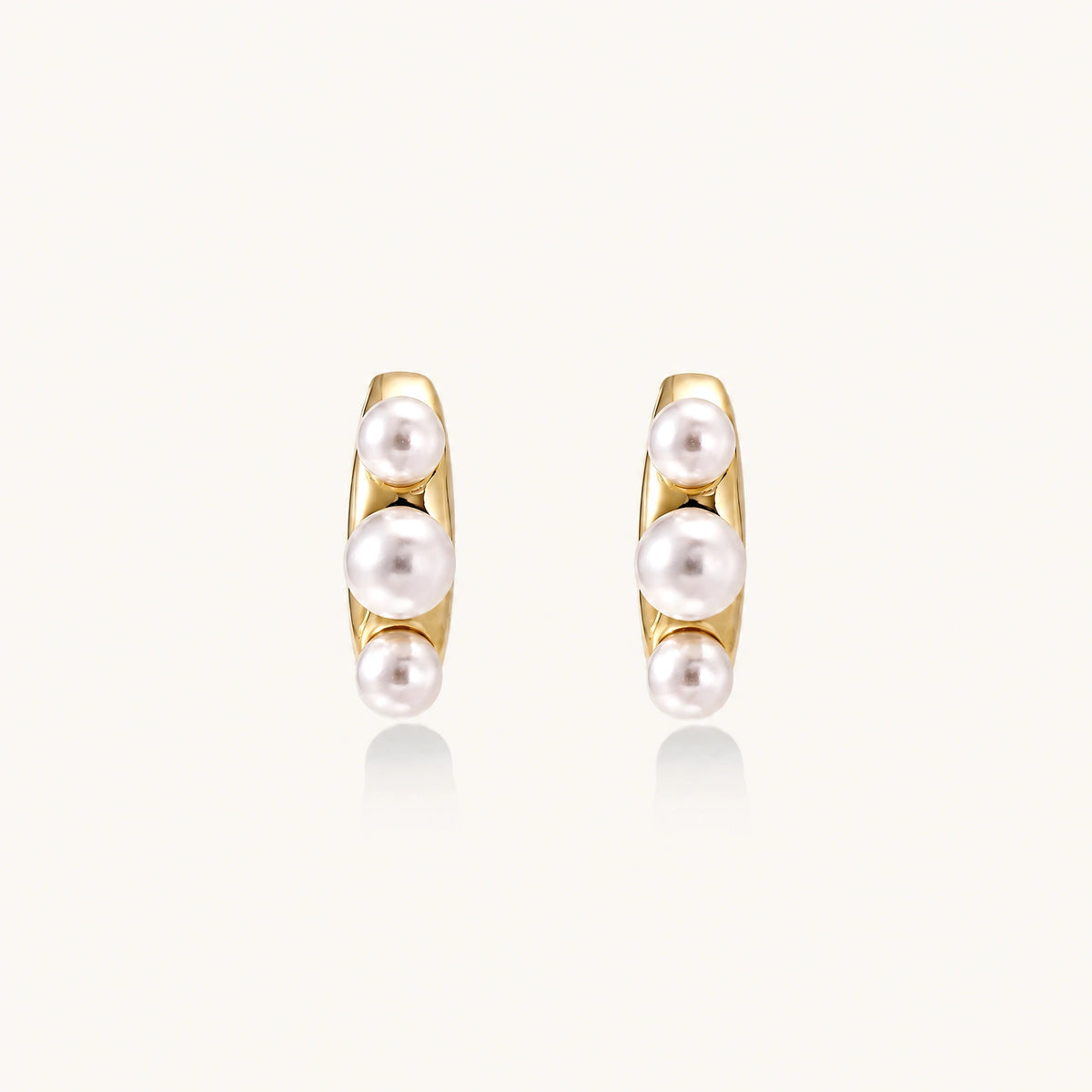 14K gold-plated curved stud earrings with three white freshwater pearls aligned vertically on cream background