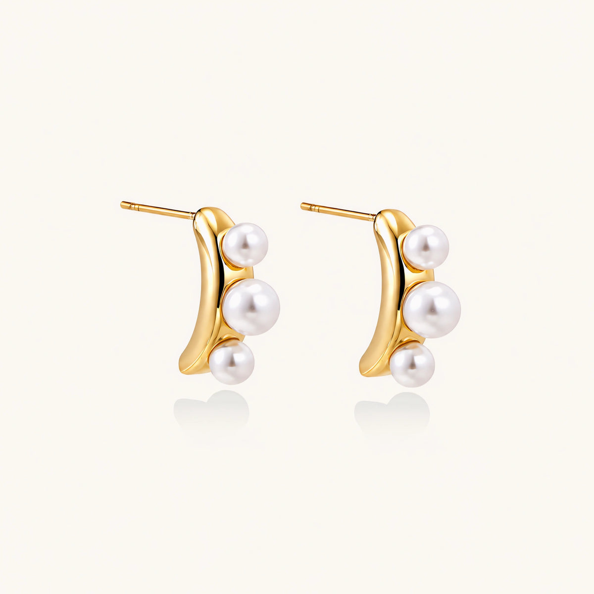 14K gold-plated curved stud earrings with three white freshwater pearls aligned vertically on cream background