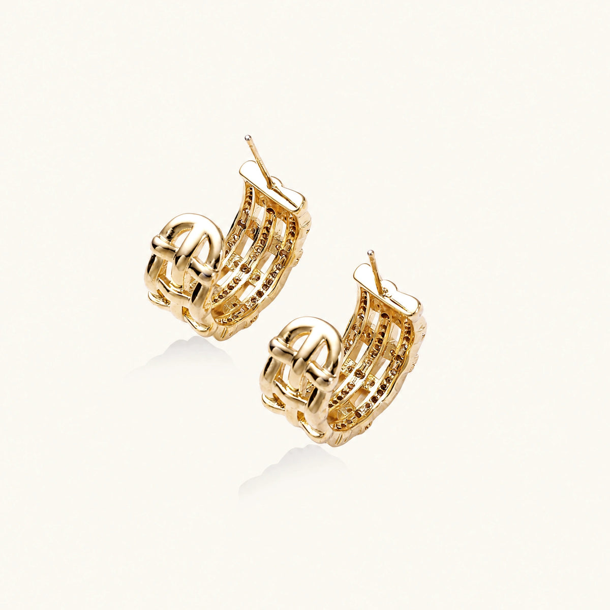 Gold-plated geometric hoop earrings with basket-weave lattice design and pavé crystal accents on cream background