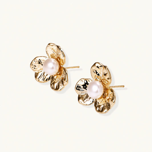 Gold-plated flower stud earrings with textured petals and centered freshwater pearl on beige background
