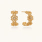 Gold hoop earrings with intricate three-dimensional floral filigree pattern in 14K gold plated brass on cream background