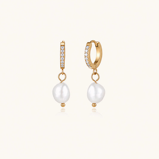 Gold huggie hoop earrings with pavé crystals and white freshwater pearl drops on cream background