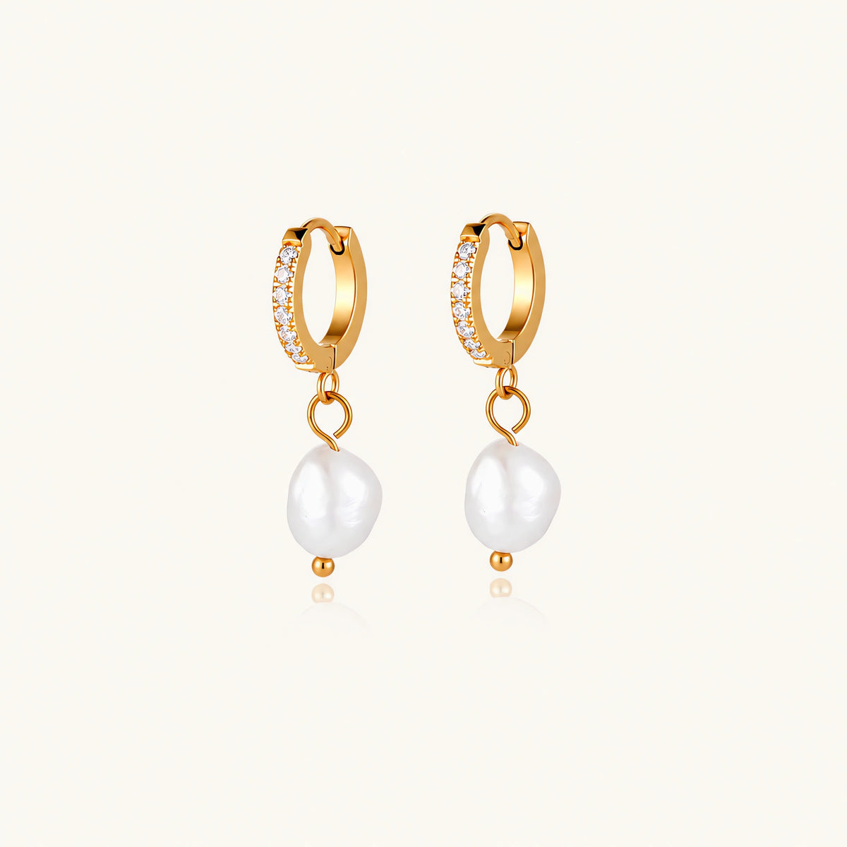 Gold huggie hoop earrings with pavé crystals and white freshwater pearl drops on cream background