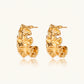 Pair of gold huggie hoops with sculpted wave texture and dimensional ripples on neutral background.