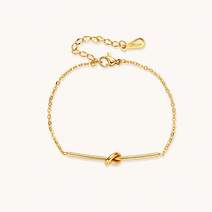 Delicate gold chain bracelet with minimalist bar and centered knot detail on cream background