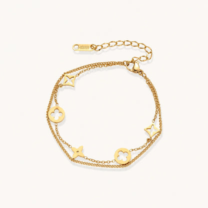 Double-layer gold-plated bracelet with quatrefoil and star charms on cream background, 18K gold finish.