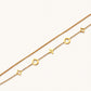 Double-layer gold-plated bracelet with quatrefoil and star charms on cream background, 18K gold finish.