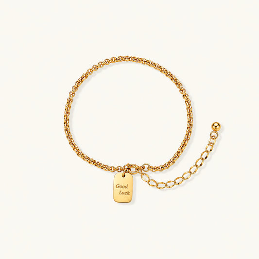 Delicate 18K gold-plated chain bracelet with Good Luck engraved rectangular pendant on cream background