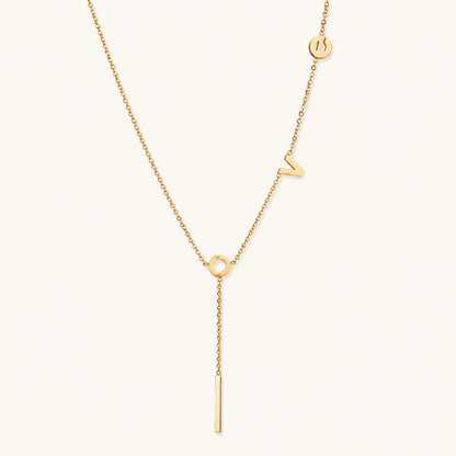 Gold Y-shaped necklace with L-O-V-E letter charms and vertical bar pendant on delicate chain against cream background