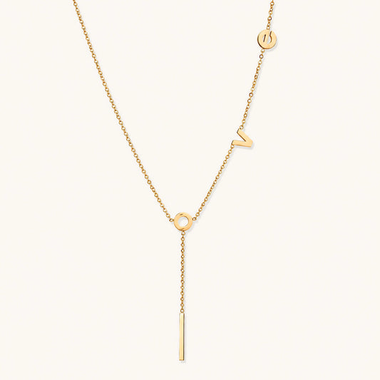Gold Y-shaped necklace with L-O-V-E letter charms and vertical bar pendant on delicate chain against cream background