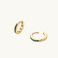 Pair of small gold huggie hoop earrings with bright green cubic zirconia stones on cream background