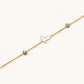 Gold chain bracelet with white mother of pearl butterfly pendant and two bezel-set crystals on cream background