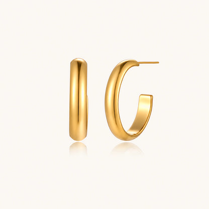 Chunky tubular hoop earrings in warm 14K gold-plated finish with smooth polished surface on cream background.