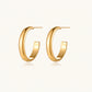 Chunky tubular hoop earrings in warm 14K gold-plated finish with smooth polished surface on cream background.