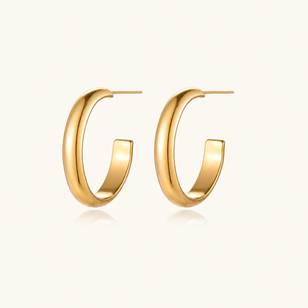 Chunky tubular hoop earrings in warm 14K gold-plated finish with smooth polished surface on cream background.