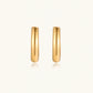 Chunky tubular hoop earrings in warm 14K gold-plated finish with smooth polished surface on cream background.