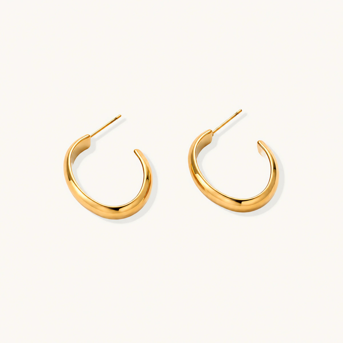 Chunky tubular hoop earrings in warm 14K gold-plated finish with smooth polished surface on cream background.
