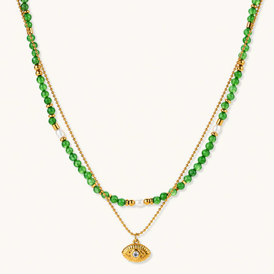 Layered necklace with green stone beads, gold spacers, white accents, and protective eye pendant on cream background.