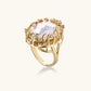 Gold filigree crown ring cradling an iridescent baroque freshwater pearl with crystal accents on white background