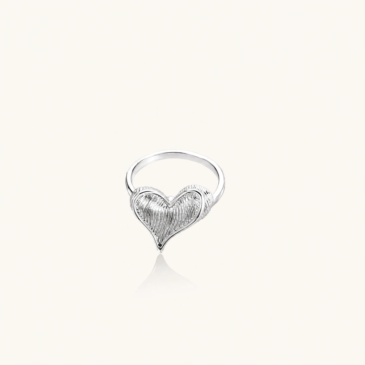 Silver ring with 3D heart formed by textured feather-like elements, white gold plated eco-brass on neutral background.