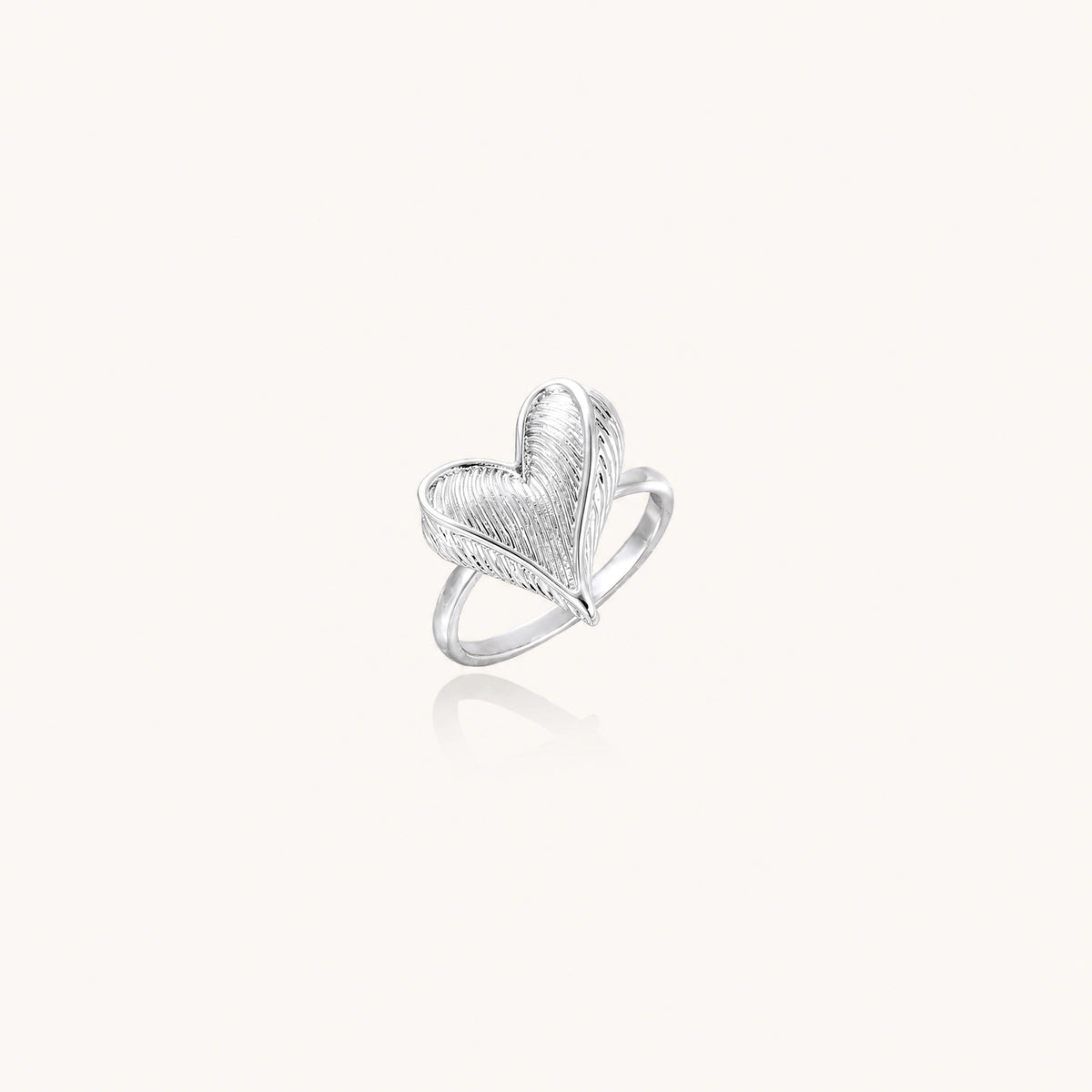 Silver ring with 3D heart formed by textured feather-like elements, white gold plated eco-brass on neutral background.