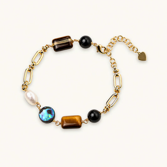 Gold chain bracelet with tiger's eye, obsidian, pearl, and iridescent abalone stones on cream background.