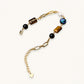 Gold chain bracelet with tiger's eye, obsidian, pearl, and iridescent abalone stones on cream background.