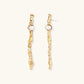 Long gold twisted sculptural earrings with round pearls, featuring flowing organic design on cream background